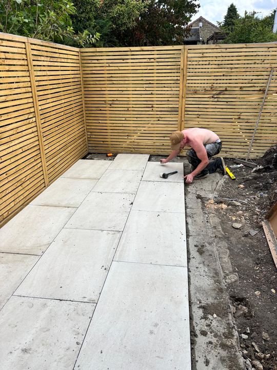 Porcelain patio tiles being laid in front of slatted fencing